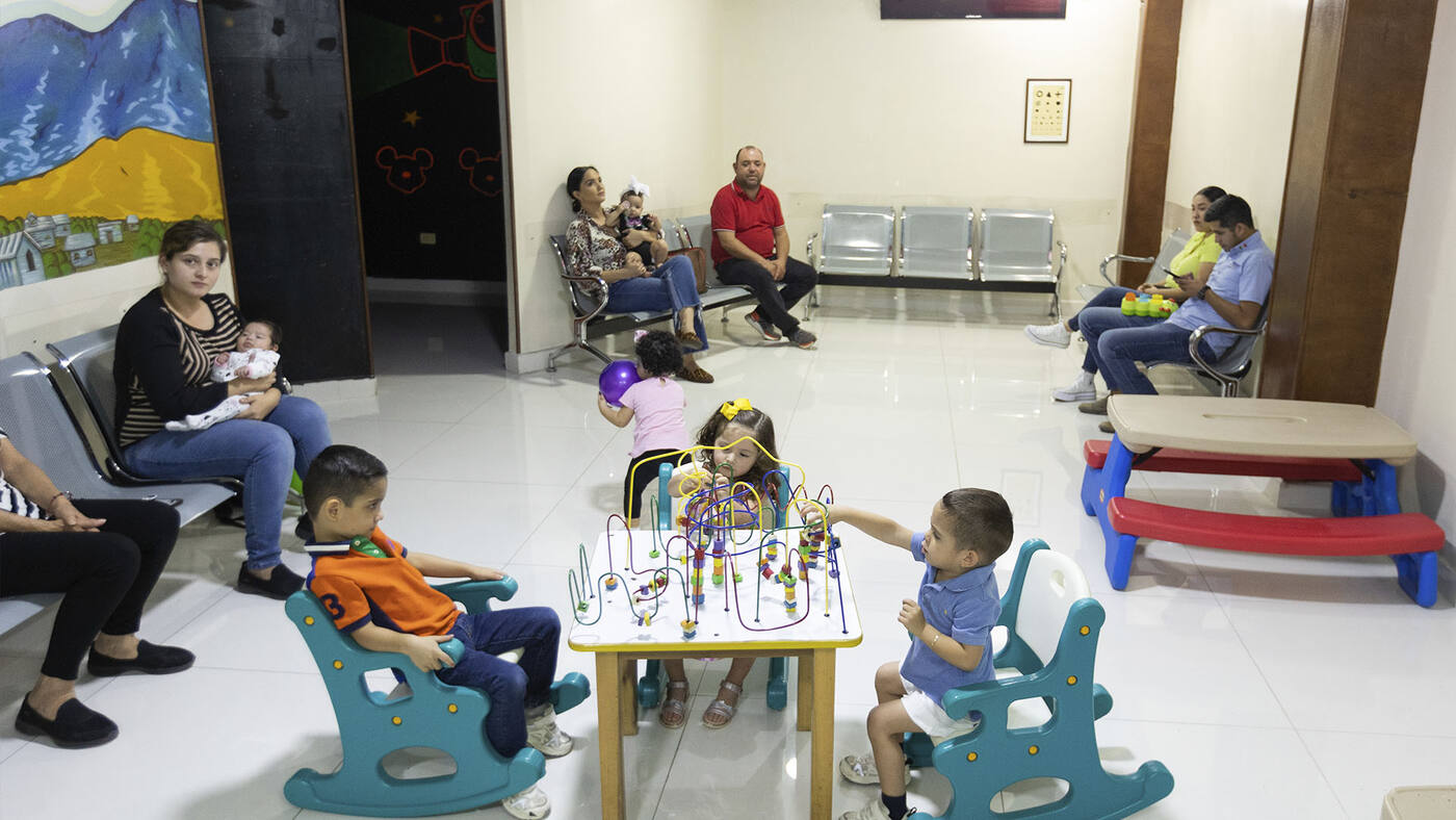 Sala de espera con niños jugando en sillitas mientras sus papás esperan